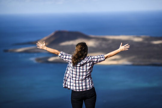 Happy woman with raised arms looking at the atlantic ocean. Lanzarote, Canary Islands.