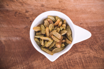 Top view image of raisin in a white cup on wooden background