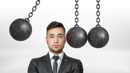 A businessman in a front view stands with his head dangerously put between several wrecking balls...