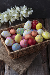 Easter basket with colored eggs and flower on a wooden table