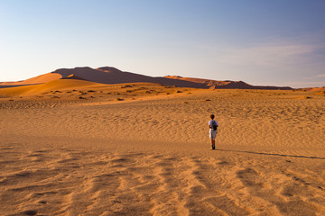 Fototapeta na wymiar Tourist walking on the sand dunes at Sossusvlei, Namib desert, Namib Naukluft National Park, Namibia. Traveling people, adventure and vacations in Africa.