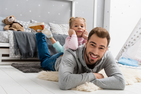 happy young father and daughter lying on floor in kid bedroom