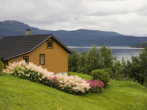 Bellos paisajes de fiordos noruegos por el lago de Sorfjorden . Casa típica amarilla, con césped y flores de colores, verde, rosa, amarilla, montañas y lago. Vacaciones en Noruega verano de 2017.