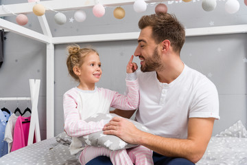 Fototapeta premium young father and happy little daughter sitting on bed in kid bedroom