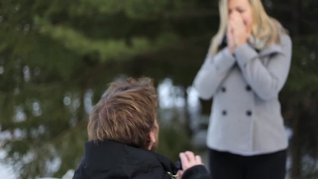 man proposes to woman on one knee ring hidden behind back