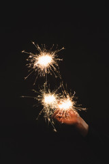 partial view of woman holding burning sparklers  in hand isolated on black