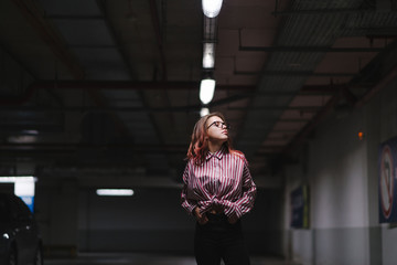 Portrait of young beautiful girl wearing stylish shirt, black skinny jeans, glasses. Girl have shinny long red hair. Female fashion concept