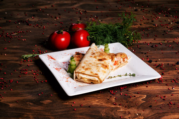 Fast food. lyulya-kebab, shaverma, pita, gyros. Tortilla with meat and vegetables. Delicious dish decorated with greens, sliced cucumbers and tomatoes served on a white plate