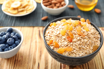 Bowl with oatmeal flakes and raisins on wooden background