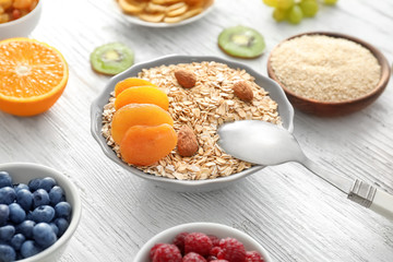 Bowl with oatmeal flakes, dried apricots and almond on wooden background
