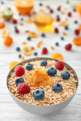 Bowl with oatmeal flakes, berries and raisins on wooden background