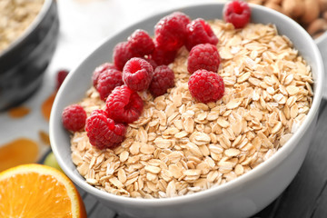 Bowl with oatmeal flakes and raspberries on table, closeup