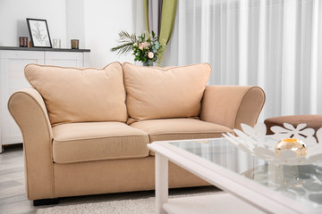 Stylish sofa with glass table in interior of living room