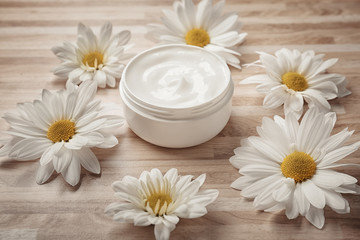 Jar of body cream and flowers on wooden background