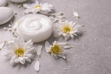 Obraz na płótnie Canvas Jar of body cream and flowers on grey background