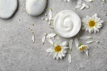 Fototapeta na wymiar Jar of body cream and flowers on grey background
