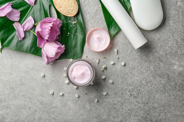 Jar of body cream and flowers on table, top view