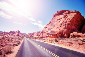 Desert road against the sun, travel concept picture with lens flare effect, color toned, Nevada, USA.