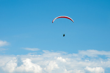Alone paraglider flying in the blue sky against the background of clouds. Paragliding in the sky on a sunny day.