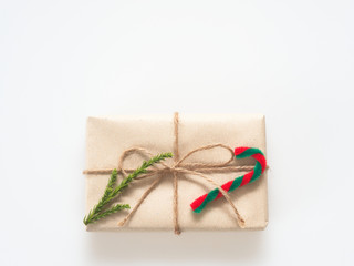 A present or gift box wrapped by rough brown recycled paper and tied with brown hemp rope ribbon with pine branch and candy cane isolated on white background with green and eco freindly concept