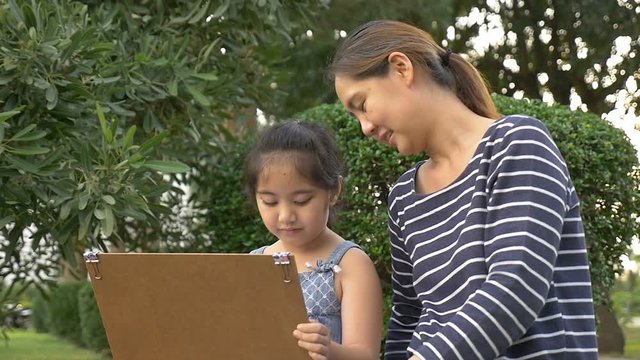 Slow motion of Happy Asian Daughter drawing picture with mother together in the park