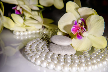 Fototapeta na wymiar flat stones on a white glass on the background of yellow orchids 