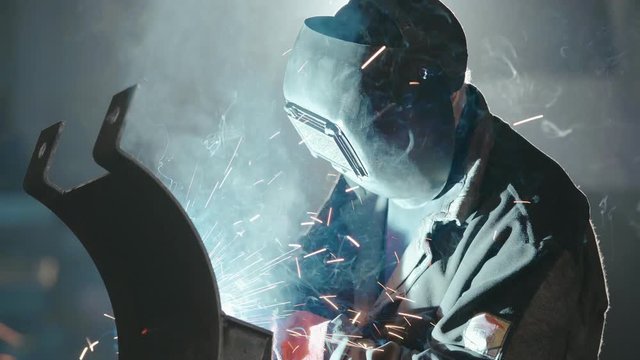 Man industrial welder in protective mask welding metal parts on sparks background