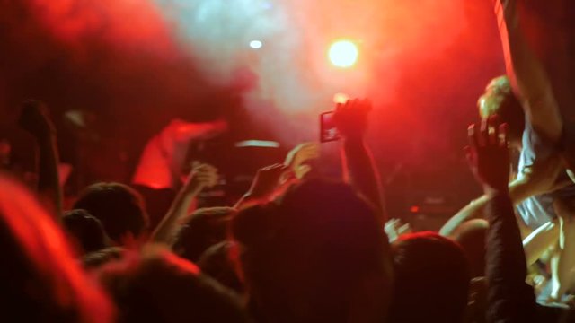 People partying and clapping in front of the stage. Unrecognizable hands silhouette taking photo or recording video of music concert with smartphone. Photography, entertainment and technology concept