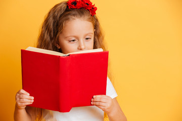 Concentrated little pretty girl reading book looking aside.