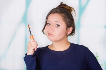 Close up of worried young woman doing a mess using a eye mascara in her eye, in a blurred background