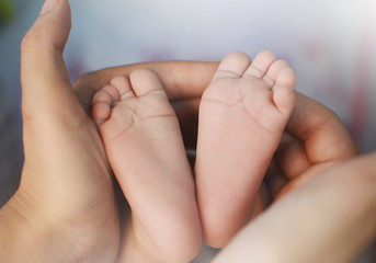 Children's legs in the hands of the mother. Tiny legs of a newborn baby on female hands close-up. Mom and her baby. The concept of a happy family. Concept of health. The treatment