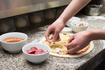 Cook in the kitchen putting the ingredients on the pizza. Pizza concept.