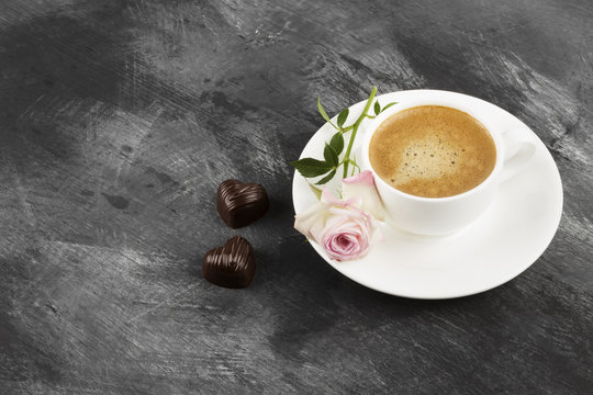 Espresso coffee in a white cup, a pink rose and chocolates on a dark background. Copy space