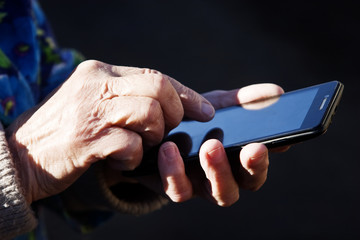 Old wrinkled hands write a message on the phone on a dark background