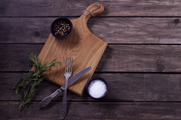 Mock up for restaraunt menu or recipe. Wooden cutting board with salt and pepper fork and knife on the gray rustic background. Copy space
