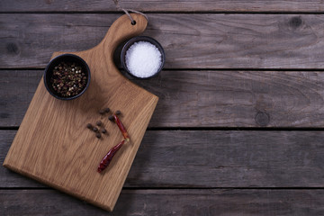 Mock up for restaraunt menu or recipe. Wooden cutting board with salt and pepper on the gray rustic background. Copy space