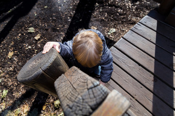 A Caucasian Toddler Plays On A Wooden Play Structure In A Public Park