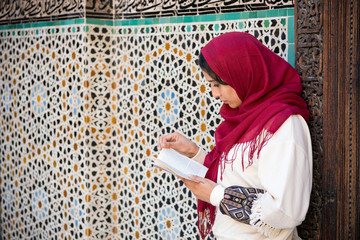 Arab woman with red hijab on her head reading a book