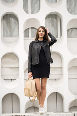 Fashion young woman in a black rock on a white wall background