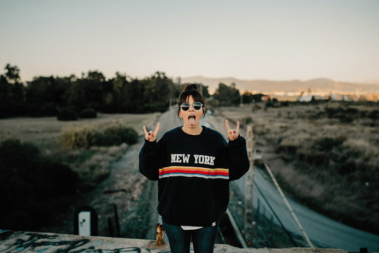 Portrait of young woman making rock on hand gesture and sticking out tongue
