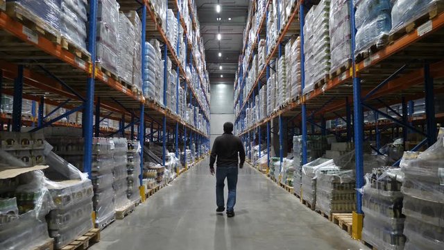 Man walking along multi level warehouse with cardboard boxes arranged on the racks