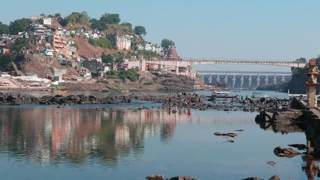 Omkareshwar cityscape, India, sacred hindu temple. Holy Narmada River, boats floating. Travel destination for tourists and pilgrims.