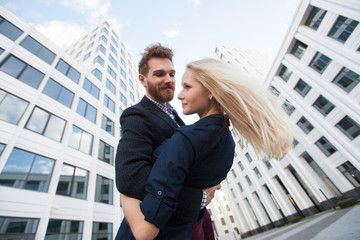 Man and woman hugging and laughing in front of a white building. Bottom view