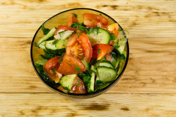 Fresh salad with tomato, cucumber, onion, parsley and dill in glass bowl on wooden table