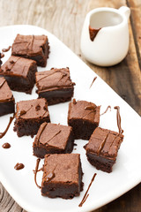 Sliced brownies on white plate. With chocolate fudge topping. Served on wooden table.