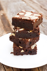 Brownies sliced with almond sliced topping on white plate. Multi layer of brownie look like tower. Served on wooden table.
