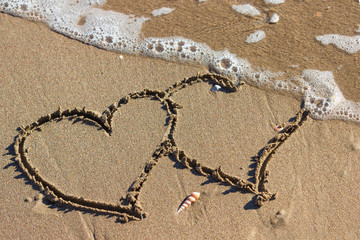 Two hearts in the sand on the beach. Waves with foam blue  sea on a sunny sandy beach in resort on summer vacation rest.
