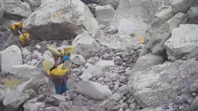 Worker carries a basket with pieces of sulfur on his shoulder. Sulfur miners carries sulfur from inside the crater of Kawah Ijen volcano in East Java, Indonesia.