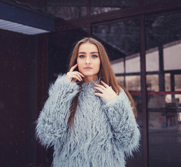 Outdoor portrait of a young beautiful fashionable lady wearing stylish fur coat.