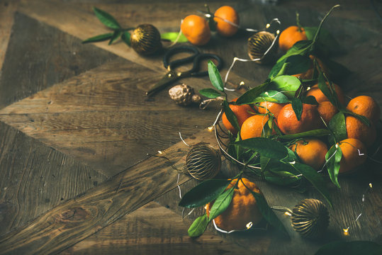 Christmas or New Year table. Fresh tangerines with leaves, decoration toys, scissors and light garland over rustic wooden table background, copy space